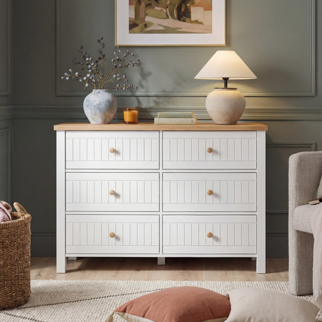 [White] Linra 6-drawer chest front view in a wider bedroom shot with lamp, vases and framed artwork above