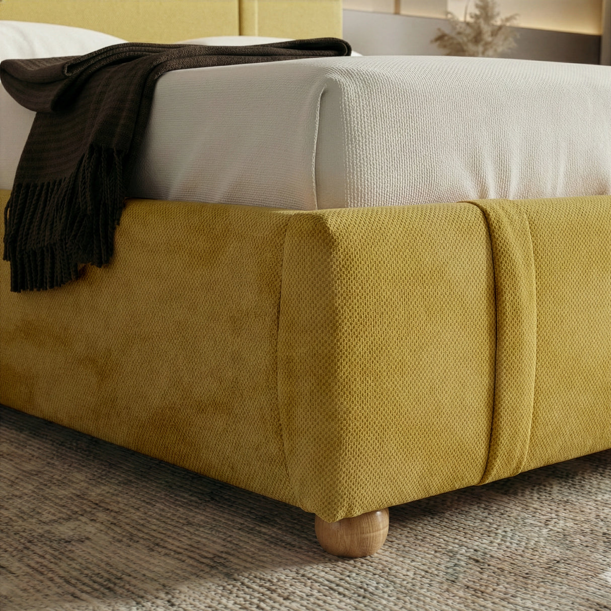 Lower corner of the yellow upholstered base with a rounded edge and a short wooden foot of the king bed frame