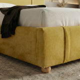Lower corner of the yellow upholstered base with a rounded edge and a short wooden foot of the king bed frame