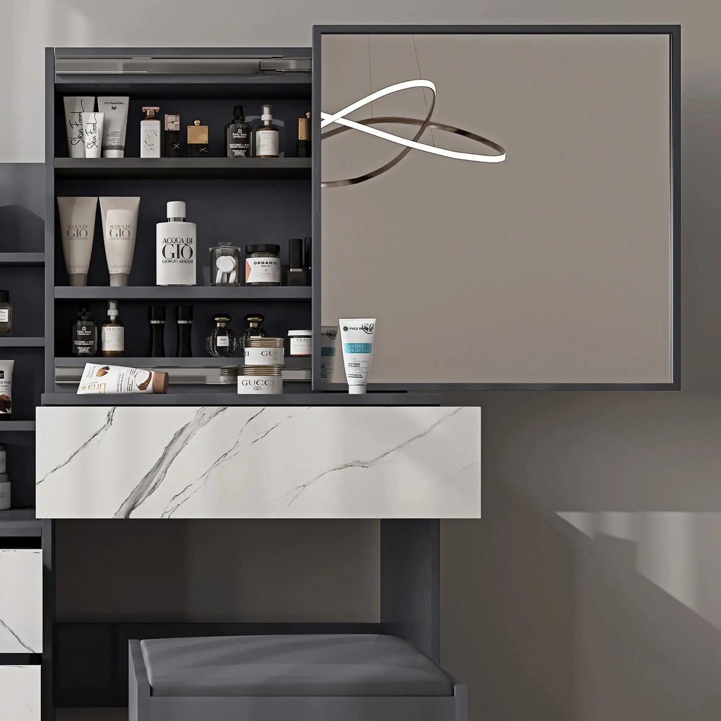 Grey vanity table with large mirror and marble drawer. Features open shelving and ample storage for beauty products in a modern bedroom setup.