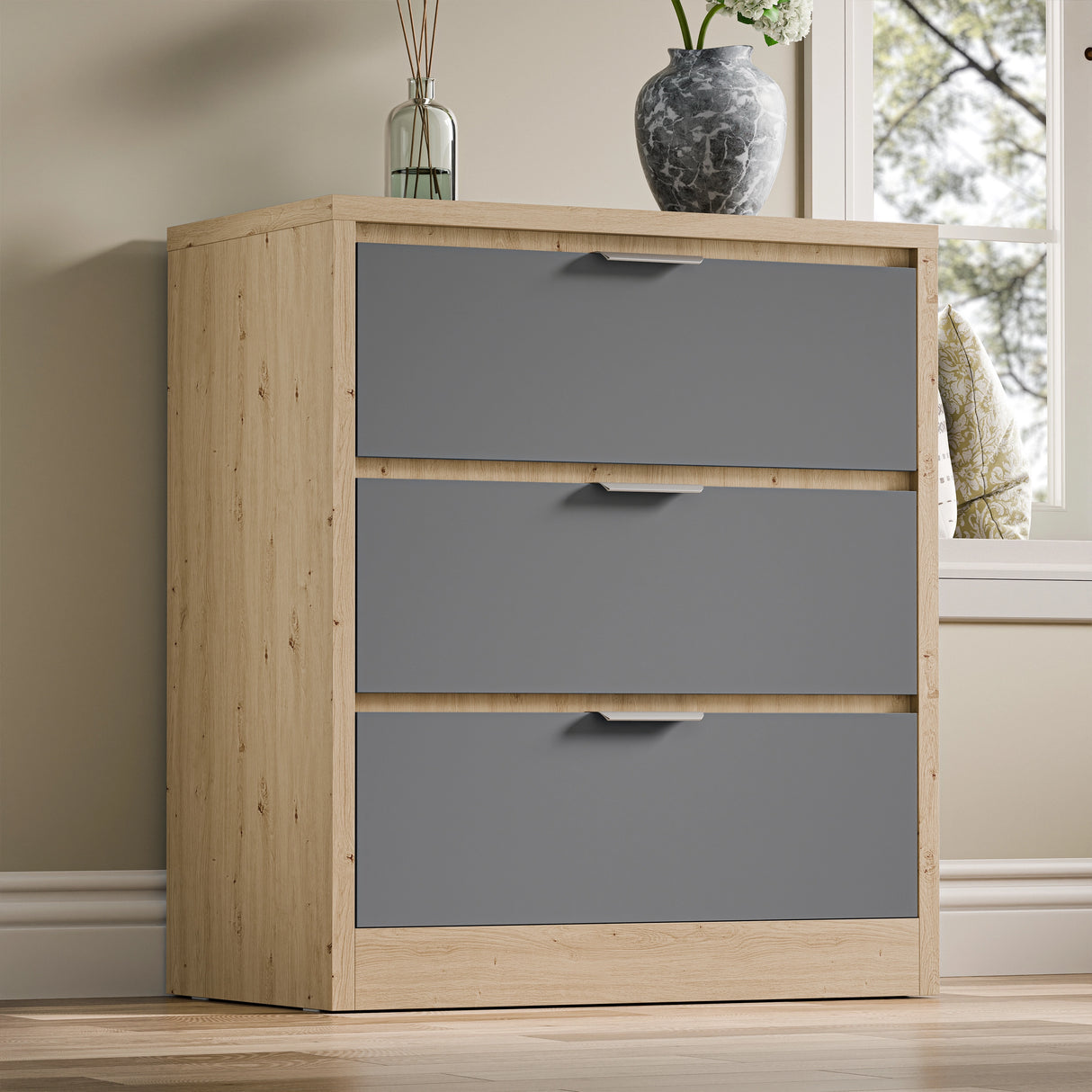 Three-drawer chest of drawers in two tone finish, placed against a wall near a window in a natural light setting