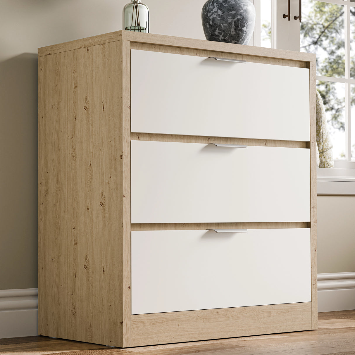 Skova chest of drawers, a three-drawer unit in white and wooden finish, placed against a wall in natural light near a window