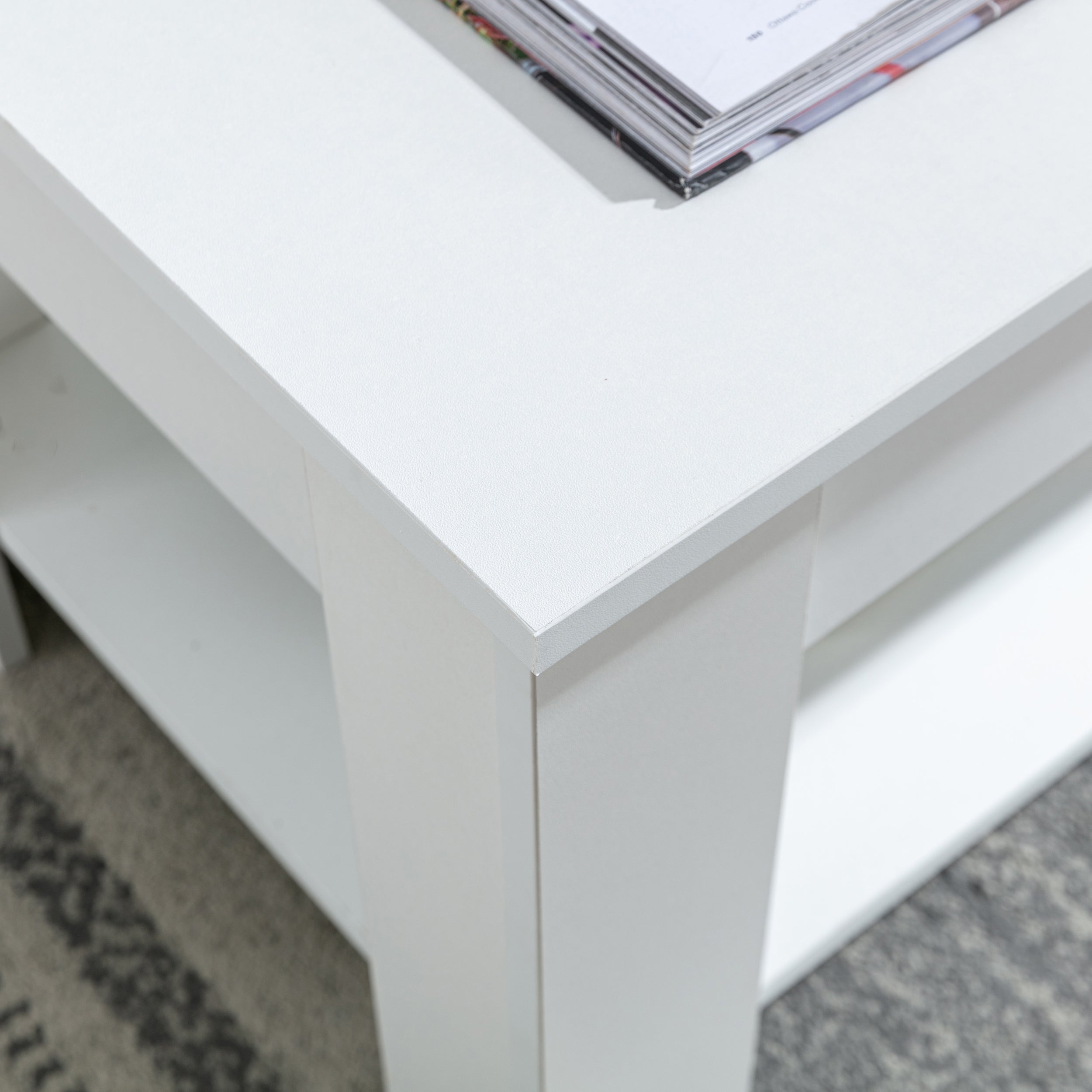 Close-up of the edge and surface of a white coffee table with a stack of magazines on top, highlighting its modern design.