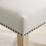 [Beige | Set of 2] Close-up of fabric seat, bronze nailhead trim and light wooden leg on the dining chair