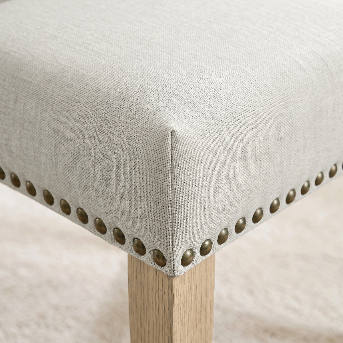 [Beige | Set of 2] Close-up of fabric seat, bronze nailhead trim and light wooden leg on the dining chair