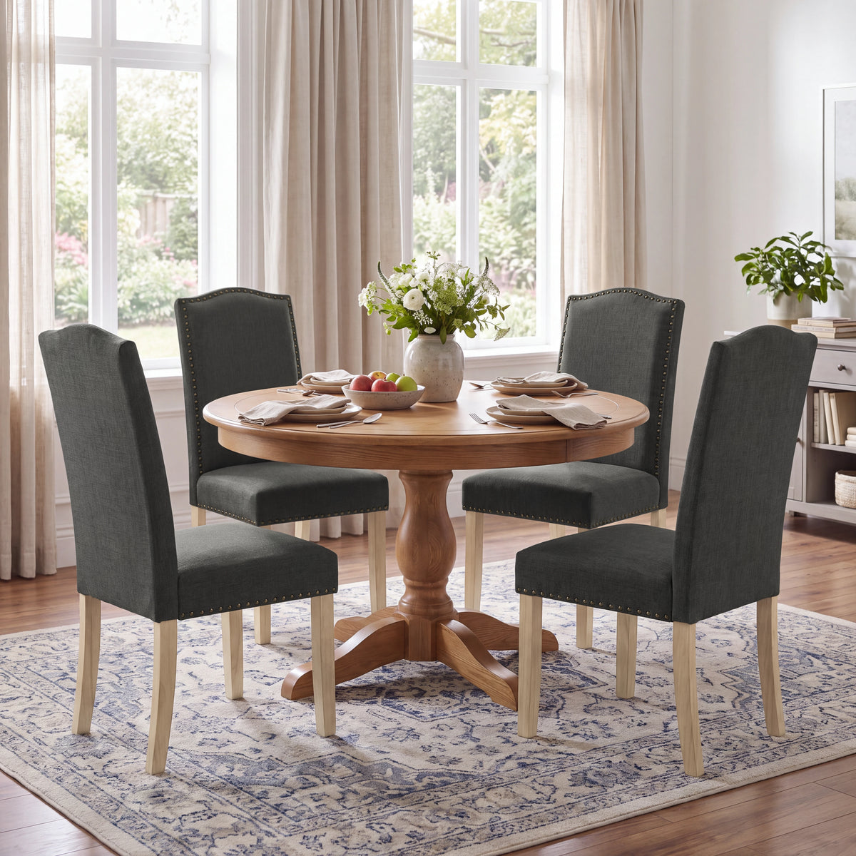 [Dark Grey | Set of 4] Four nailhead dining chairs shown around a round wooden dining table in a dining room