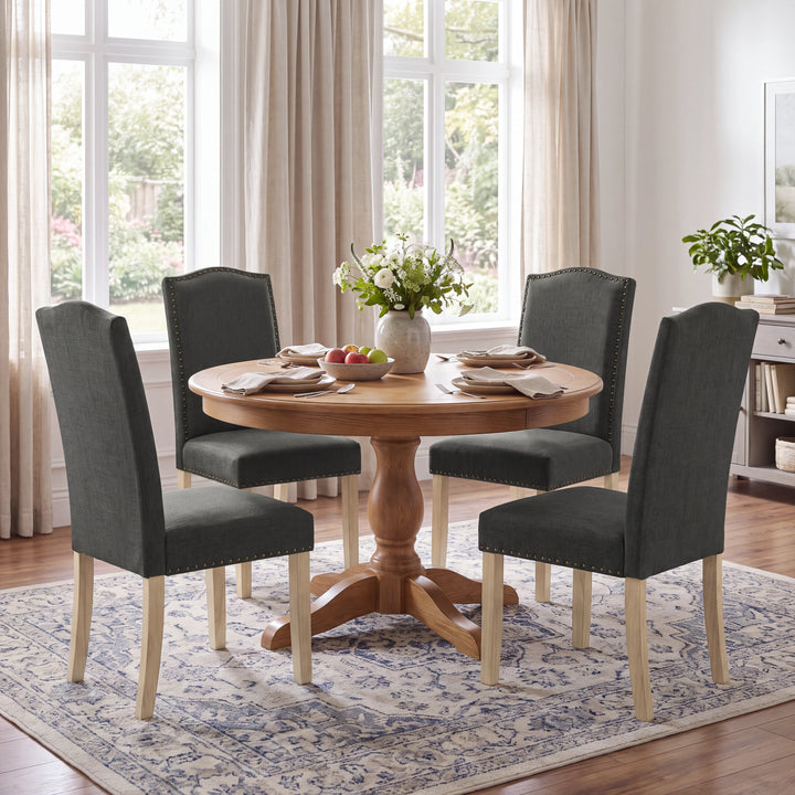 [Dark Grey | Set of 4] Four nailhead dining chairs shown around a round wooden dining table in a dining room