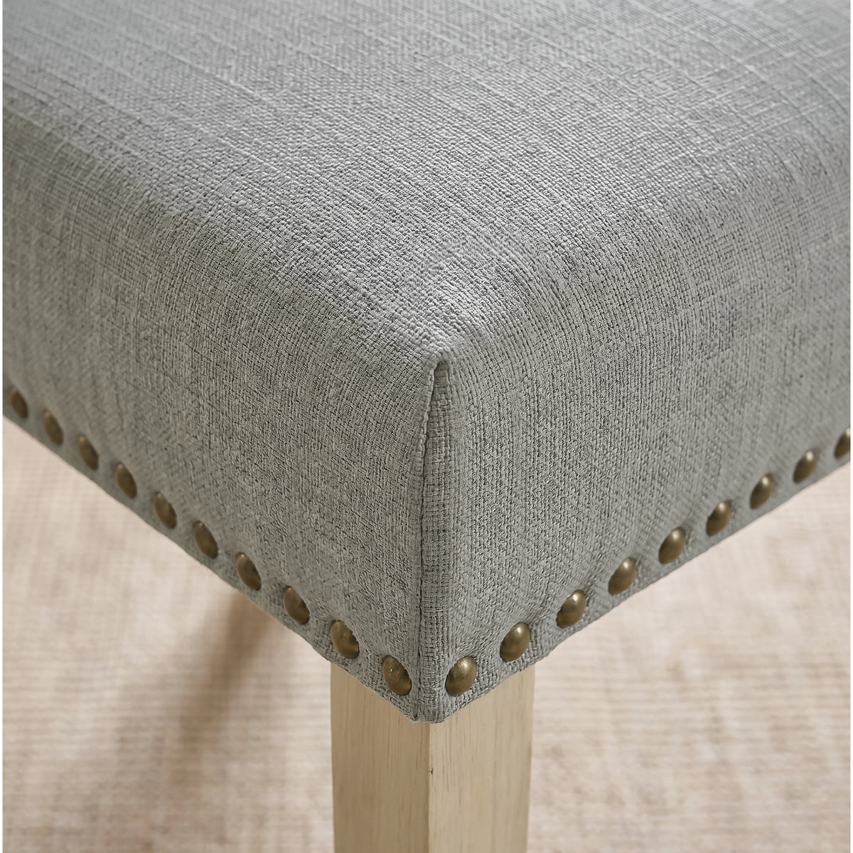 [Light Grey | Set of 2] Close-up of fabric seat, bronze nailhead trim and light wooden leg on the dining chair