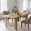 [Oak] Closed oak-effect dining table styled with fruit, flowers and candles; beige chairs stand by its thick legs.