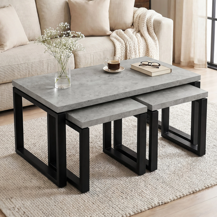 [Concrete] Nestline table set beside a cream sofa, with vase flowers, book, and black nesting frames below