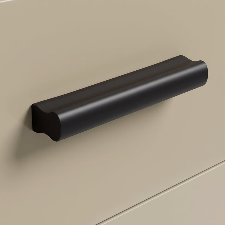 [Oak+Cashmere] Macro close-up view of the smooth black matt drawer pull handle mounted on a beige matt drawer front panel