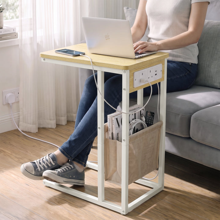 [Oak] C-shaped side table used for laptop work by sofa with charging station plugged in wall socket and storage pouch