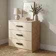 [Oak + Cashmere] Wooden dresser with three drawers, a lamp, books, and a plant in a room with a neutral color scheme.