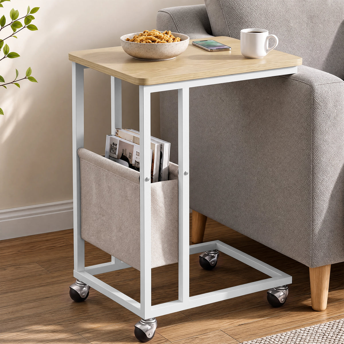 [Oak] sofa side table side view with oak-effect top, storage pouch, snacks and wheeled C-shaped base