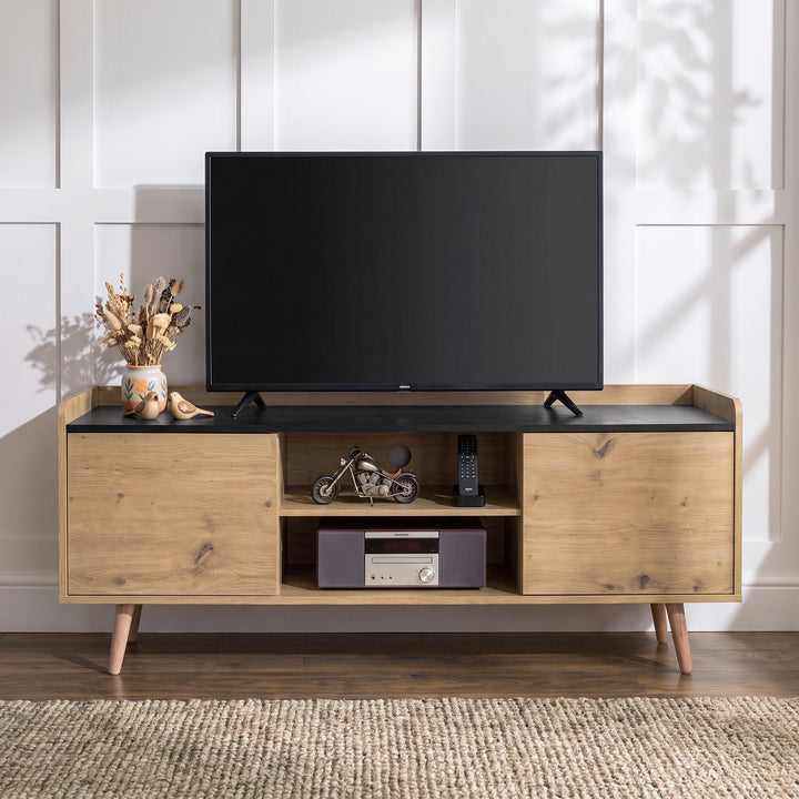 [Oak] modern wooden TV stand with a black top surface, styled with a black-screen TV, decorative items, and a stereo receiver, set against a white paneled wall.