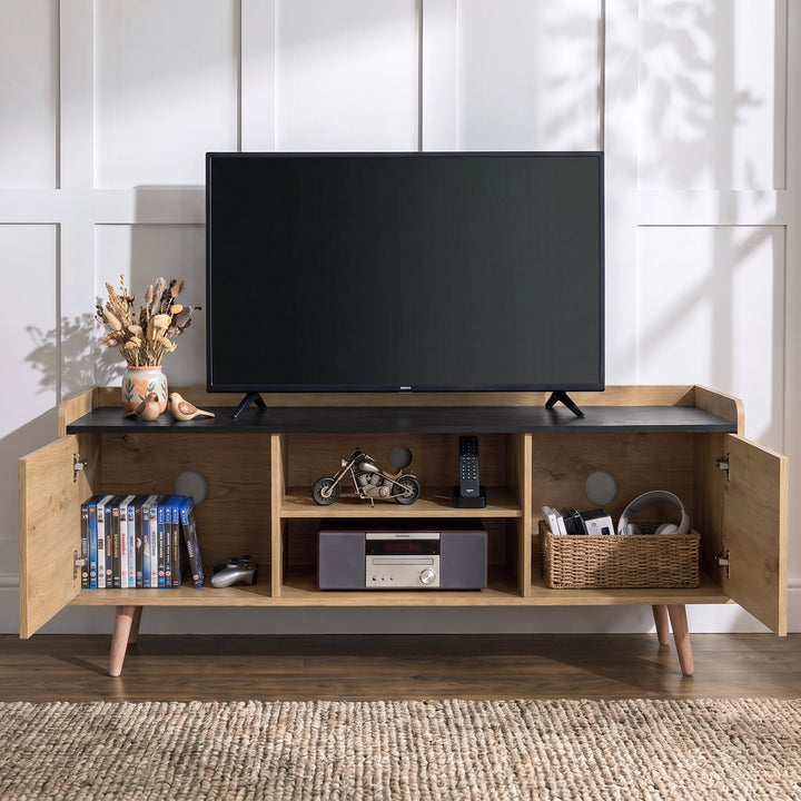 [Oak] TV stand with open side cabinets and open center shelves, styled with a black TV, DVDs, a motorcycle model, a radio, and a basket on a woven rug in a bright room.