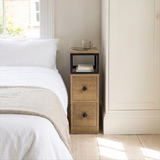 [Oak] Narrow side table with storage beside a bed, holding a lamp and small bedroom essentials
