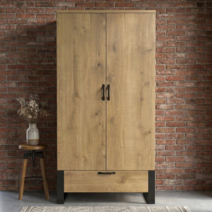 [Oak Effect] Rustvale wardrobe front view with closed double doors, lower drawer, black frame legs, brick wall, and stool.