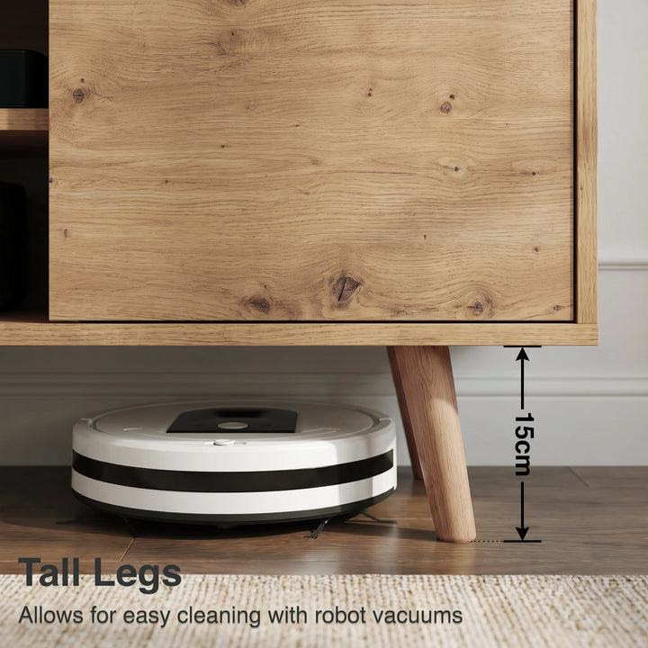 [Oak] Larvik close-up of 15cm tapered oak legs with robot vacuum passing underneath on wooden floor in warm-toned room