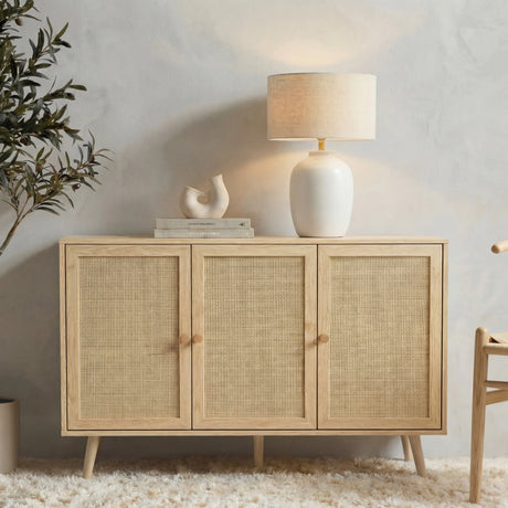 [Oak Effect] Wovena 3-door sideboard in a front lifestyle view against a grey wall, topped with a round ceramic lamp, sculptural vase, and stacked books beside a wishbone chair