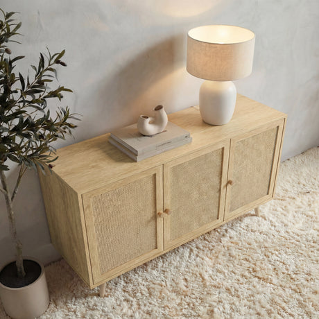 [Oak Effect] Wovena 3-door sideboard seen from above in a textured grey room with a lit ceramic lamp, sculptural vase on stacked books, and an olive tree to the left