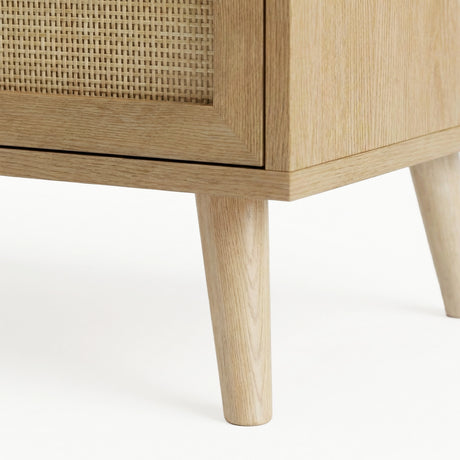 [Oak Effect] Wovena close-up of two solid tapered oak legs where they meet the cabinet base, with rattan door panel visible at the top left