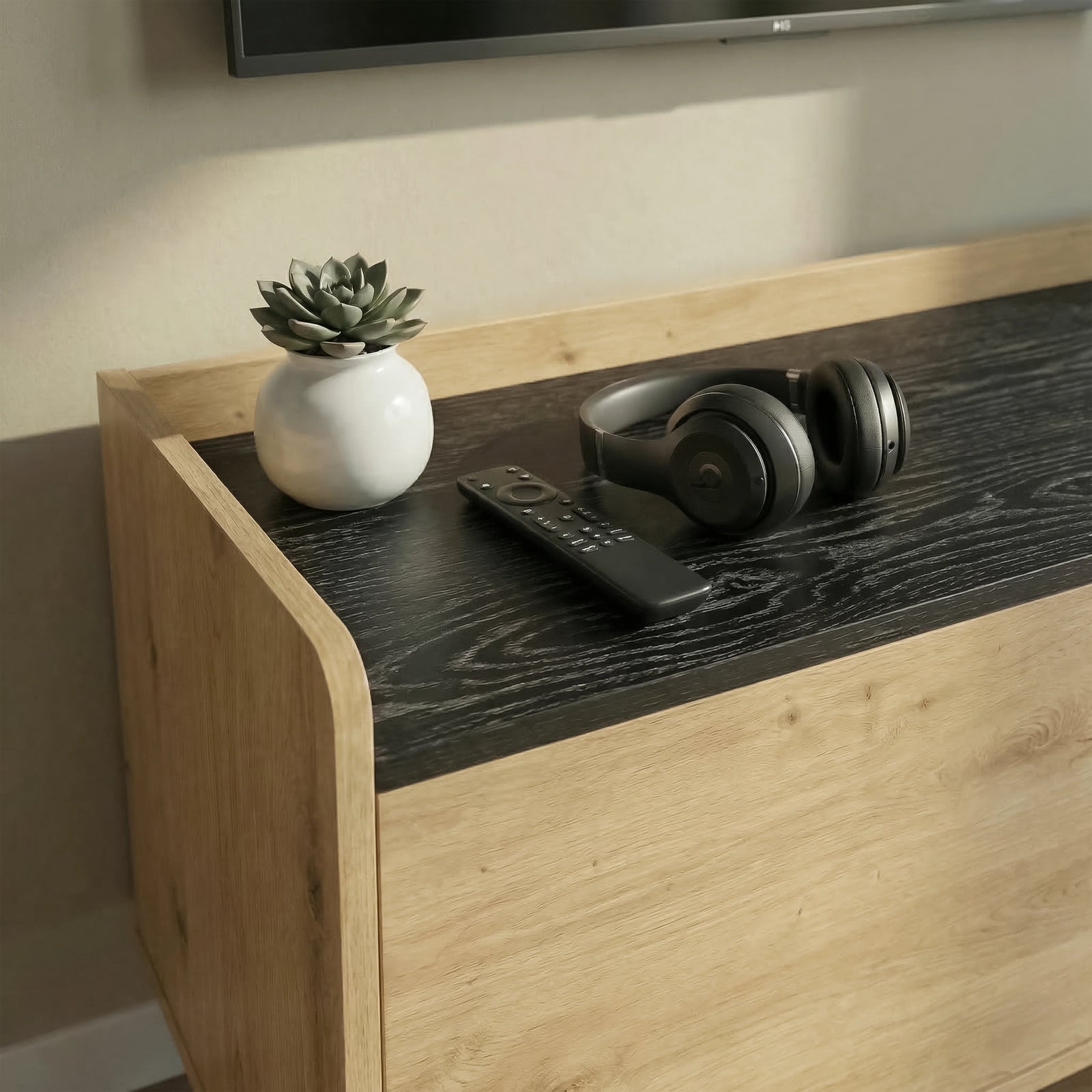 [Oak] Larvik close-up of dark woodgrain top surface with succulent pot, remote control, and headphones beside curved oak side edge