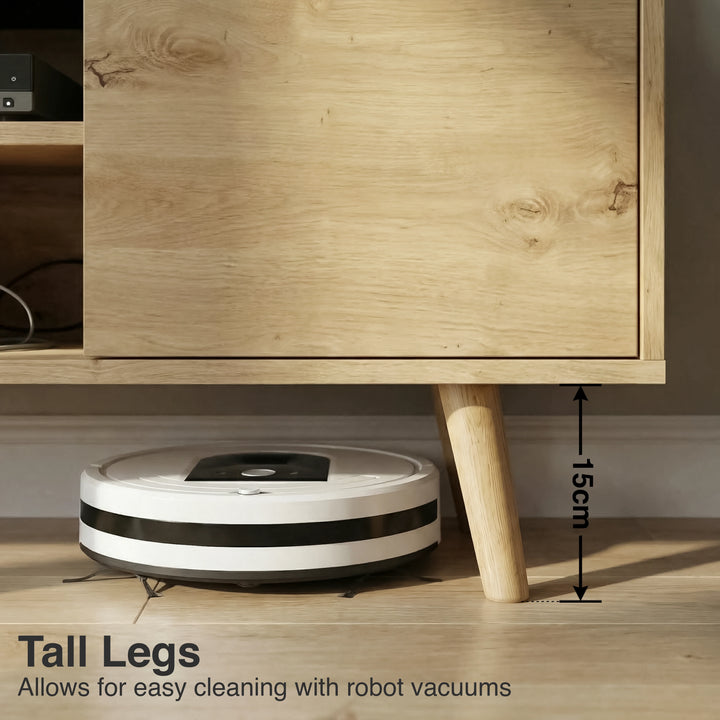 [Oak] Larvik close-up of 15cm tapered oak legs with robot vacuum passing underneath on wooden floor in warm-toned room