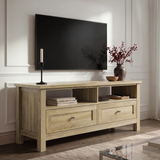 [Oak] Oskara TV unit in a bright living room below a wall-mounted TV with open shelves holding books and media device beside red berry vase