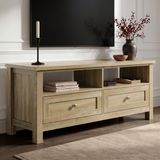[Oak] Oskara TV unit angled view in living room below a TV with two open shelves, shaker drawers, candlestick, and red berry vase on oak top