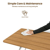 [Oak] Torvi dining table easy-clean surface detail showing person wiping the warm oak-effect MDF tabletop with a cloth on a white background
