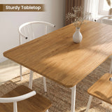 [Oak] Torvi dining table overhead close-up showing warm oak-effect tabletop surface with a small white vase and white metal arm chairs around it