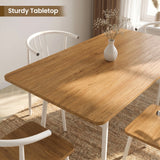 [Oak] Torvi dining table overhead close-up showing warm oak-effect tabletop surface with a small white vase and white metal arm chairs around it