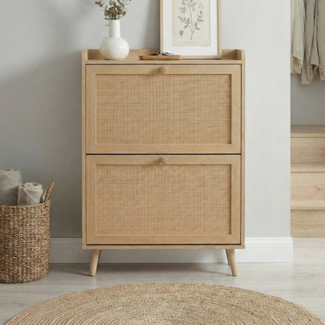 [Oak] Wovena shoe cabinet front view with closed rattan flip drawers, tapered legs, and top shelf styled with white vase and botanical print in hallway setting