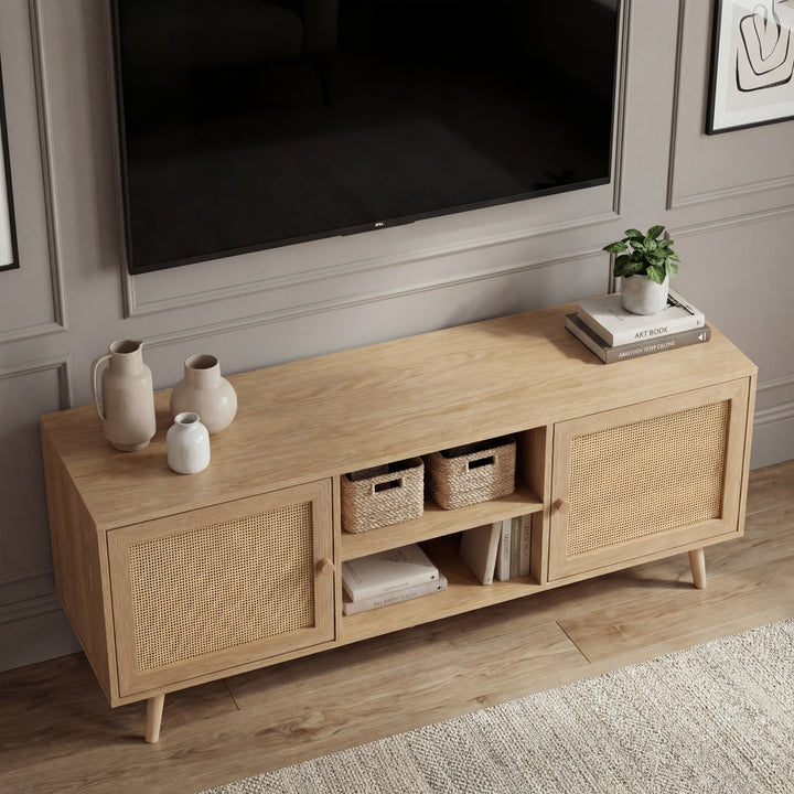 [Oak] Wovena lifestyle angle with ceramic vases, woven baskets, and stacked books beneath a TV on panelled grey wall