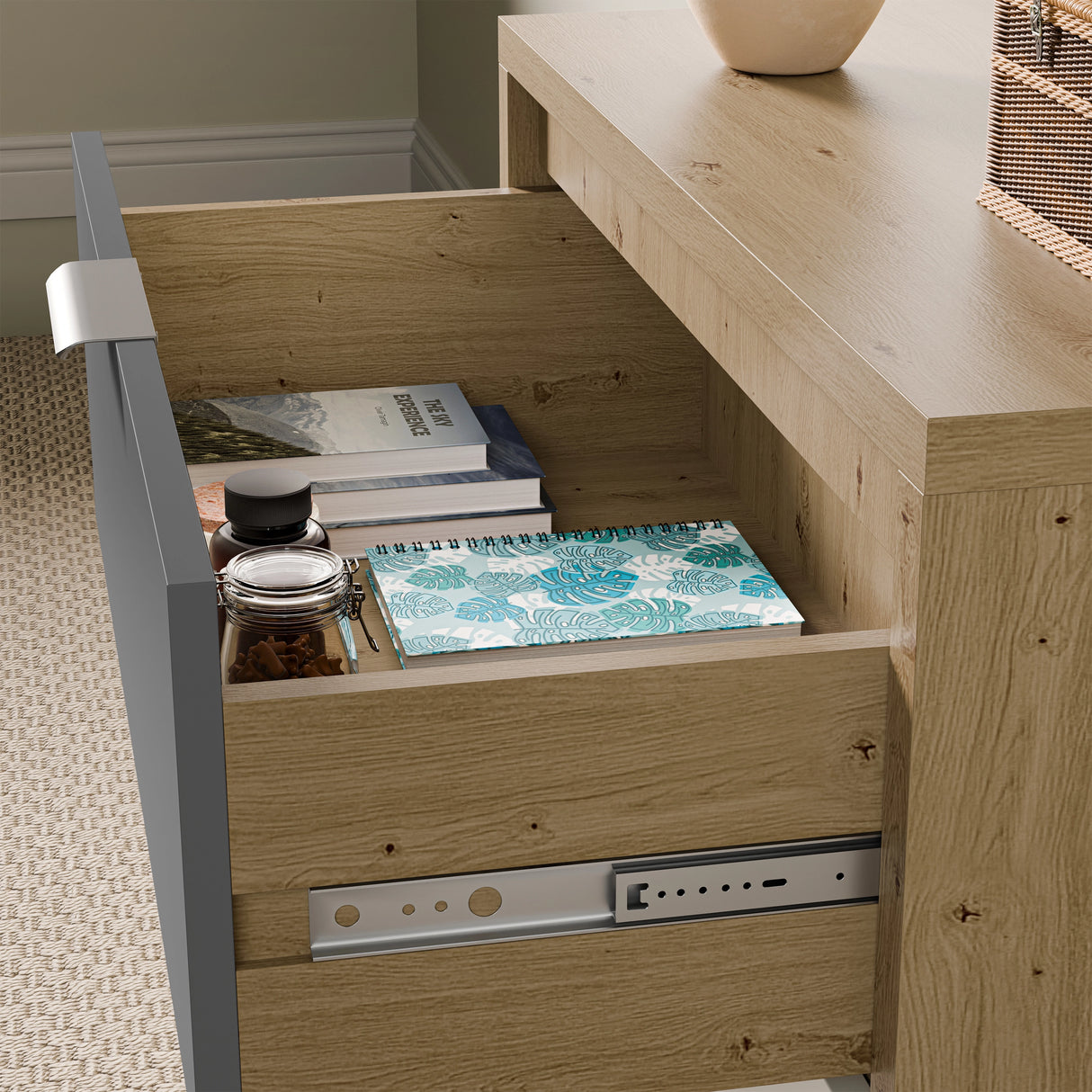 Close-up shot of a wide chest of drawers with one drawer open, showing notebooks and small jars inside