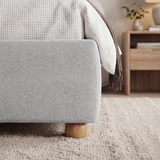[Double | Grey] Corner detail grey double ottoman bed frame showing fabric edge meeting small wooden leg on woven rug