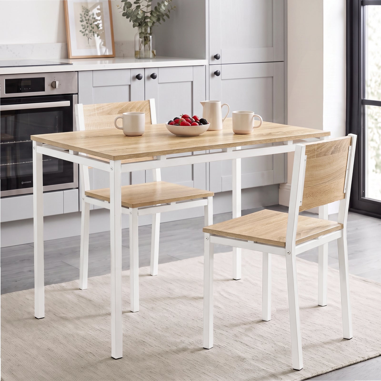 [Pine] Pine-effect breakfast table and two white metal frame chairs with mugs, bowl and cream jug in a bright kitchen diner.