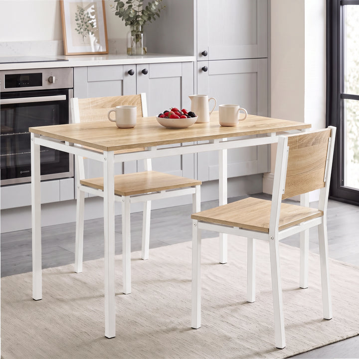 [Pine] Pine-effect breakfast table and two white metal frame chairs with mugs, bowl and cream jug in a bright kitchen diner.