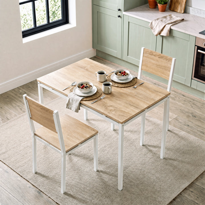 [Pine] Breakfast table and chairs for 2 styled with cereal bowls, coffee mugs and woven placemats in a bright kitchen diner.