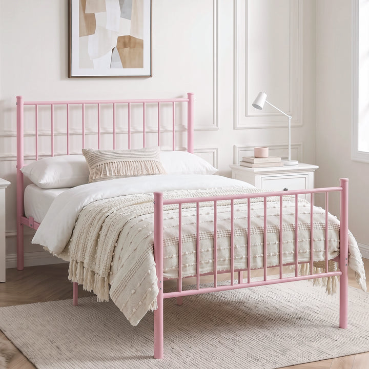 [Pink | Single] Angled view of metal bed with white bedding, beige throw, bar ends, centre leg, nightstand and reading lamp.