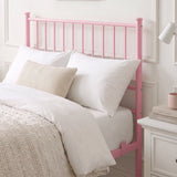 [Pink | Single] Metal bed close-up view of tall bar headboard with white pillows, beige knit cushion, lamp & bedside drawers.