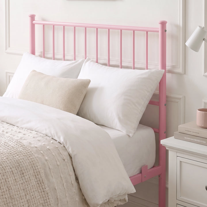 [Pink | Single] Metal bed close-up view of tall bar headboard with white pillows, beige knit cushion, lamp & bedside drawers.
