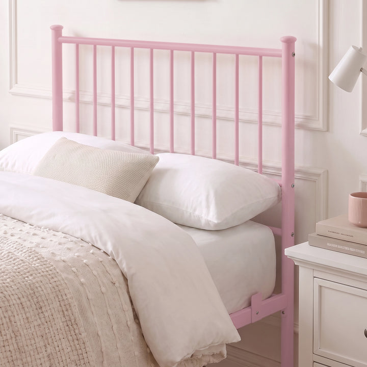 [Pink | Single] Metal bed close-up view of tall bar headboard with white pillows, beige knit cushion, lamp & bedside drawers.