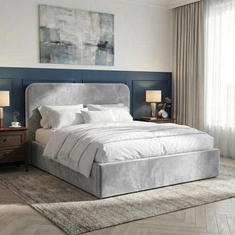 [Light Grey] Pluva velvet ottoman bed side angled view in a bedroom with dark blue wall, lamps and artwork above