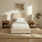 [Single | Beige] Front view of Pluva ottoman bed with curved headboard centred between matching nightstands and table lamps