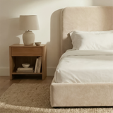 [Single | Beige] Side angle of Pluva ottoman bed showing curved headboard profile and clean velvet base beside nightstand