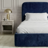 [Single | Blue] Side angle of Pluva ottoman bed showing curved headboard profile and clean velvet base beside nightstand