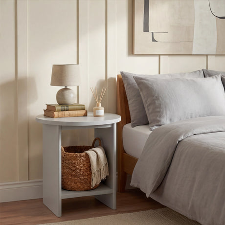 [Grey] Grey round side table used as bedside next to grey duvet bed, small lamp and books on top