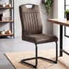 [Rust Brown] High-back dining chair by a wood table with suede-effect upholstery, carry grip and black loop metal frame.
